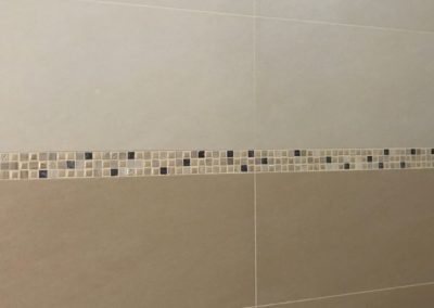 Parete del bagno con piastrelle in gres beige e fascia decoro a mosaico